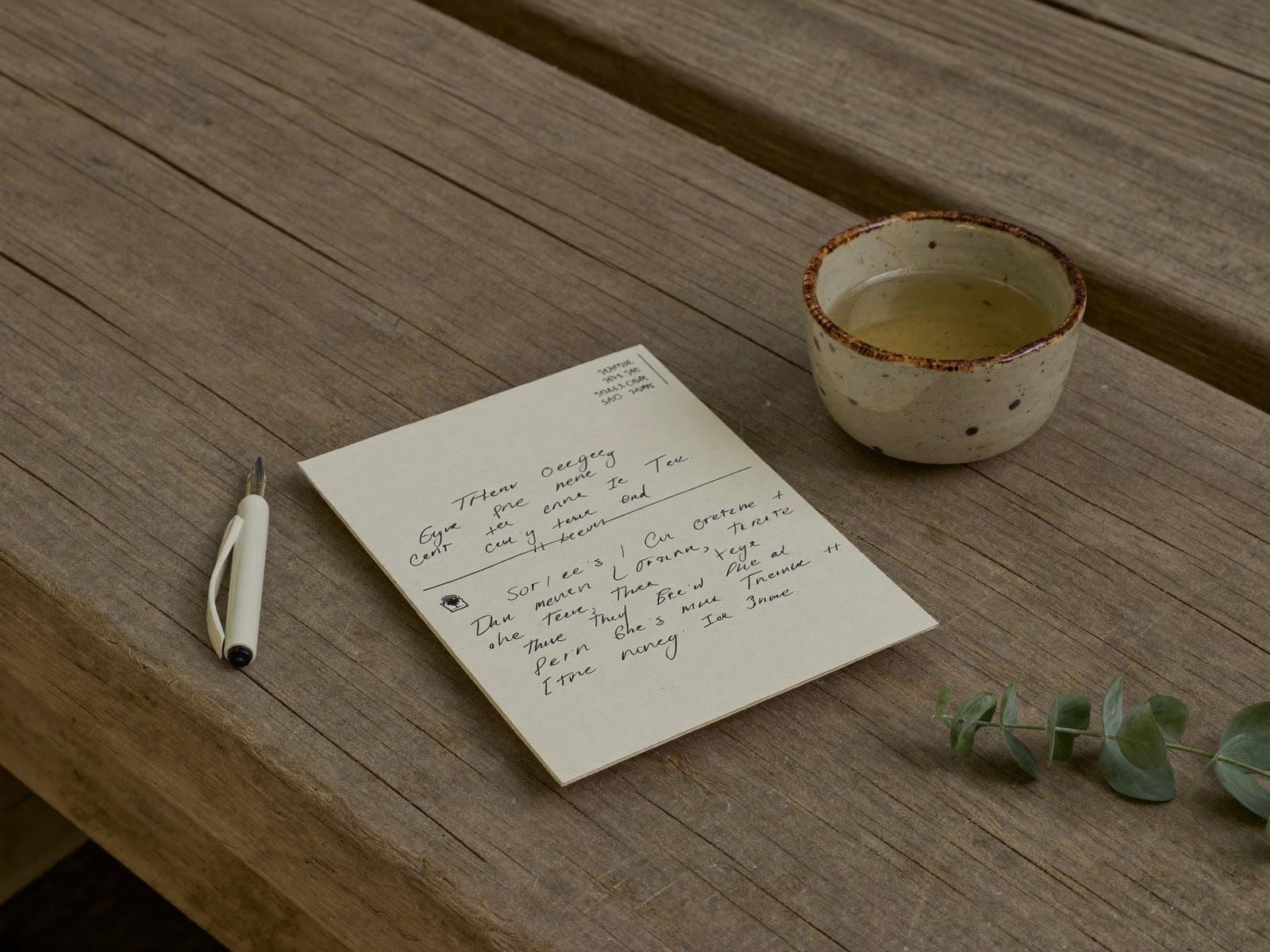 A handwritten care card, pen and ceramic cup on the timber bench