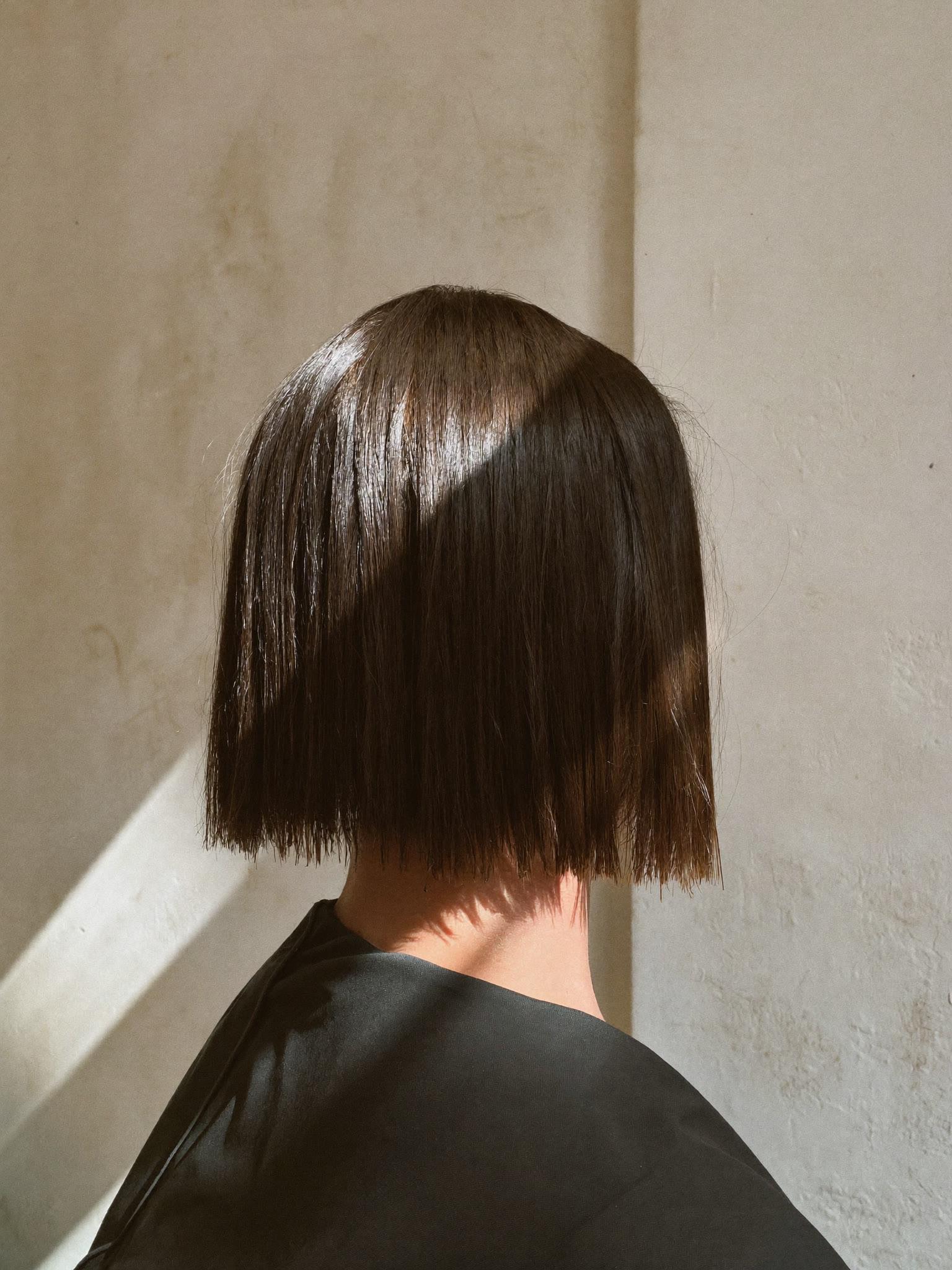 The back of a precise one-length dark bob against an ivory lime-wash wall